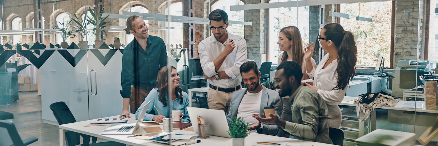 A diverse group of professionals, including graduates from top MBA in Marketing online programs, engaging in a lively discussion around a table in a modern, well-lit office with large windows and stylish décor.